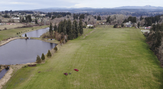 drone photo of a wide open plot of land with green grass for over 300 meters by a small body of water, more then wetlands but not as much as a lake